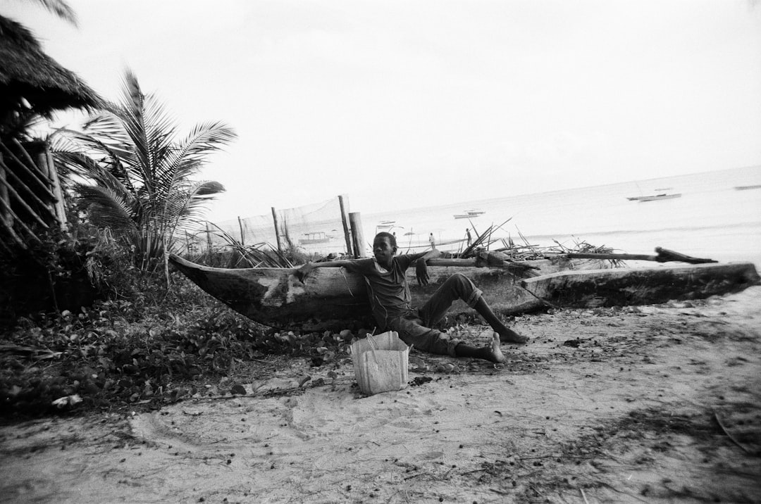 grayscale photo of man lying on wooden boat on beach shore