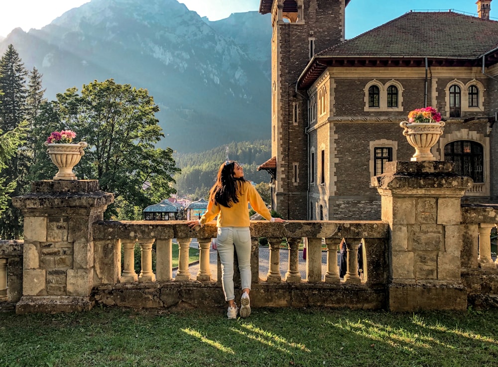 woman in yellow dress standing on green grass field near brown concrete building during daytime