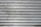 A metal roll-up shutter with horizontal slats displaying signs of rust and wear. The surface is predominantly silver with some darker smudges and spots across the slats.