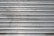 A metal roll-up shutter with horizontal slats displaying signs of rust and wear. The surface is predominantly silver with some darker smudges and spots across the slats.