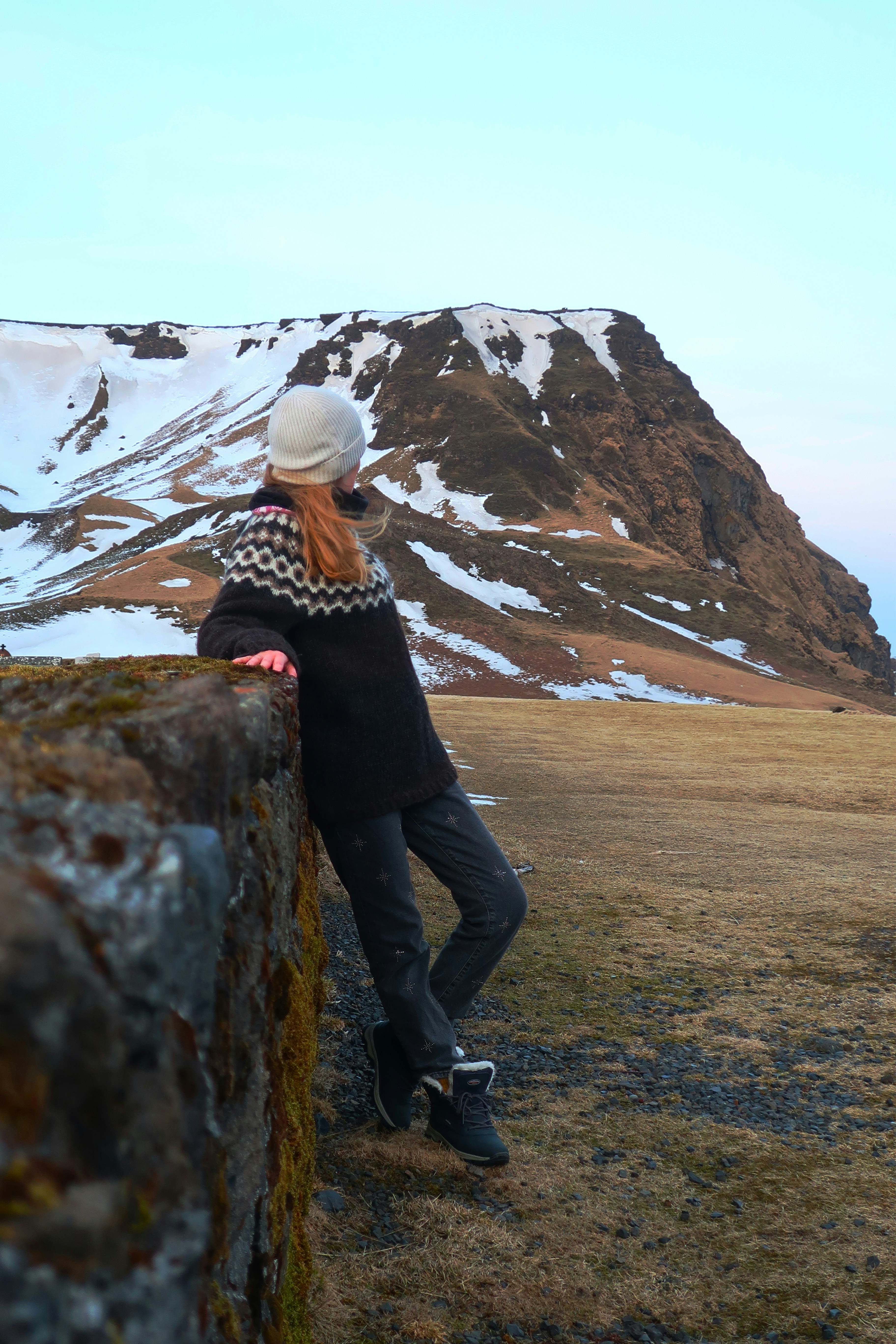 Girl wearing in lopapeysa standing near the border in front of mountain in Vik.