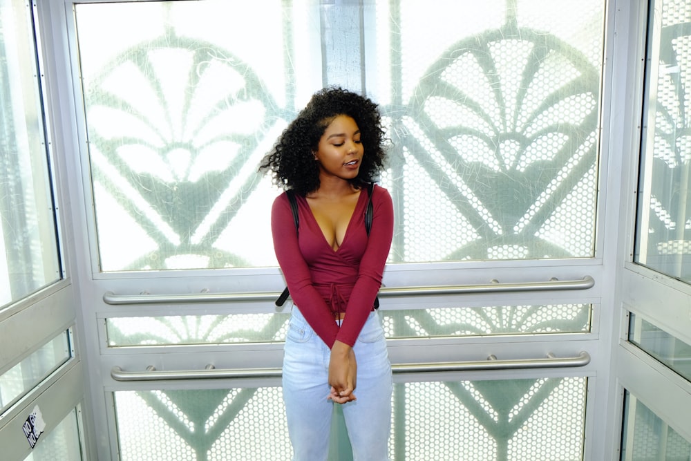 woman in red long sleeve shirt and blue denim jeans standing near white metal fence