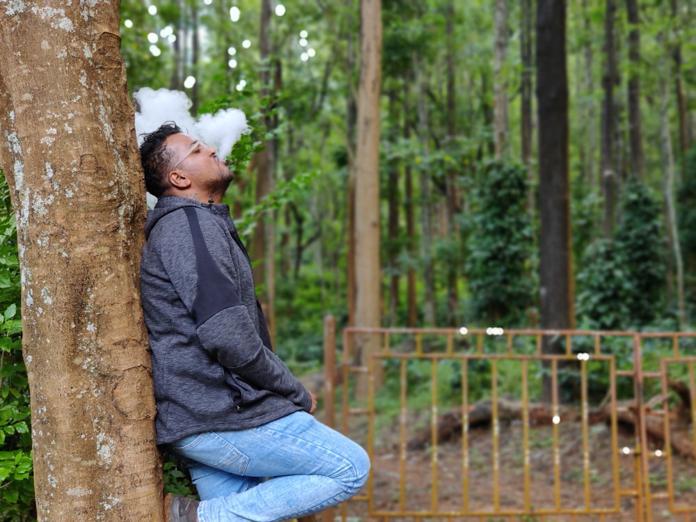 man in black jacket and blue denim jeans sitting on tree trunk