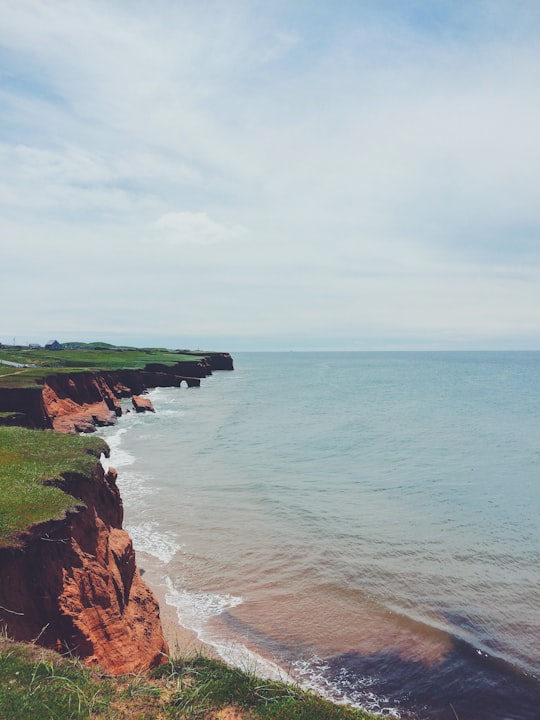 brown rock formation beside sea under white clouds during daytime in Îles de la Madeleine Canada