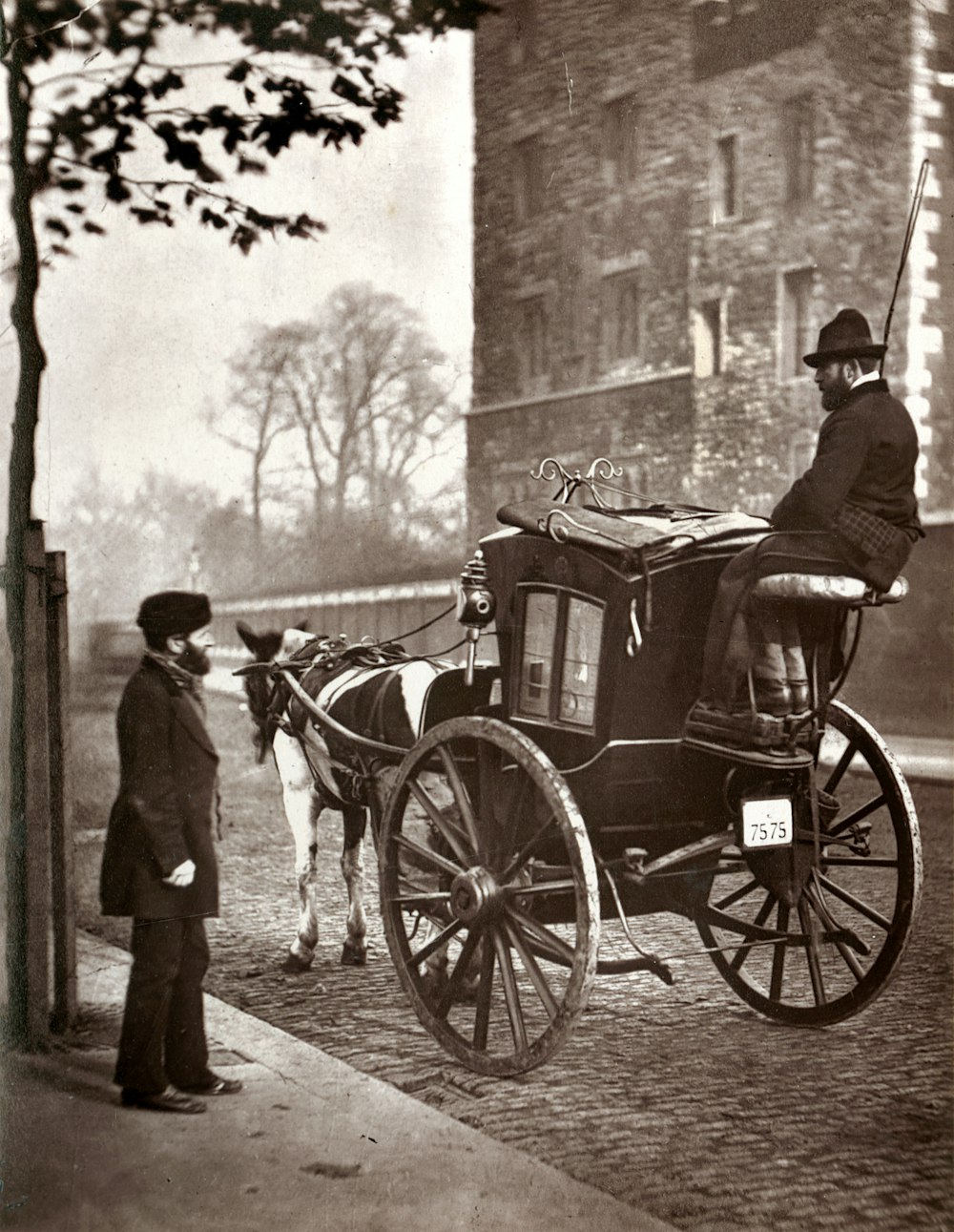 グレースケール写真で馬車の横に立つ黒いコートの男