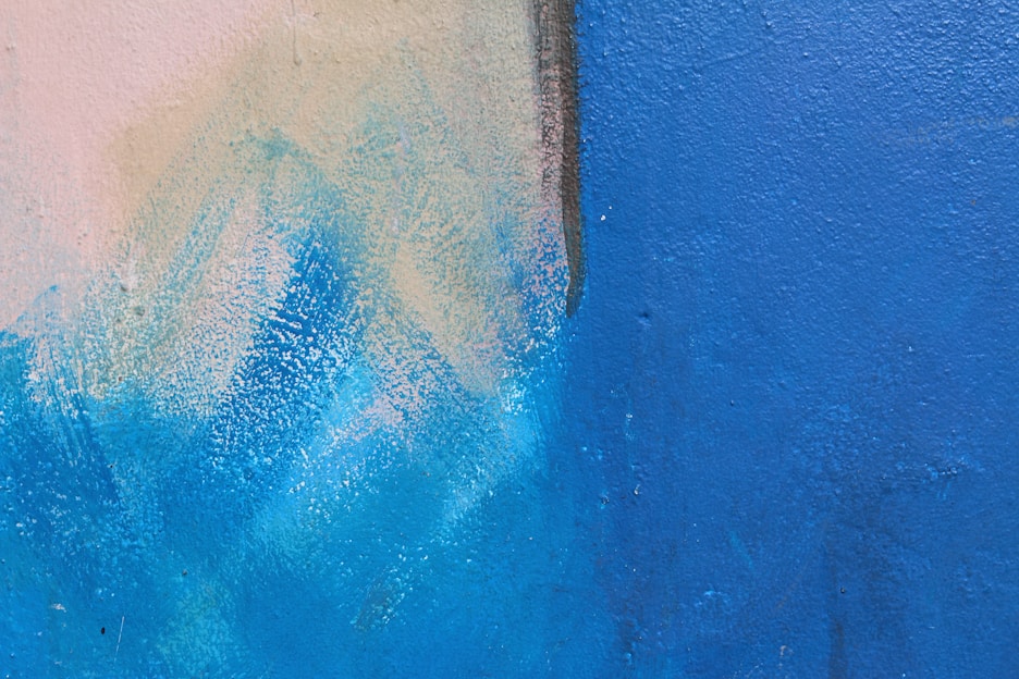 Textured painted wall featuring a blend of light beige and vibrant blue hues with a visible brushstroke pattern.