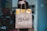 A person is holding a brown paper McCafé bag with takeaway food tags. The background indicates an indoor setting with blurred objects and decor, hinting at a casual, home-like atmosphere.