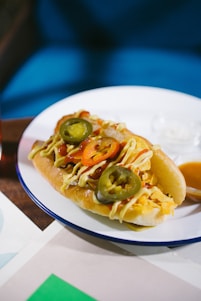 A colorful close-up of a hot dog in a jar topped with fresh ingredients and melted cheese.