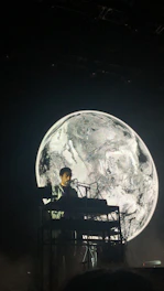A musician performing live on stage in monochrome lighting, surrounded by minimalist electronic instruments.
