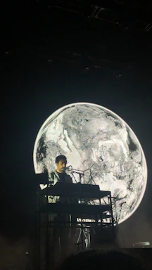 A musician performing live on stage in monochrome lighting, surrounded by minimalist electronic instruments.