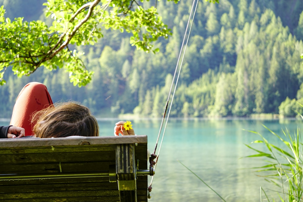 woman sitting on brown wooden bench looking at the lake during daytime