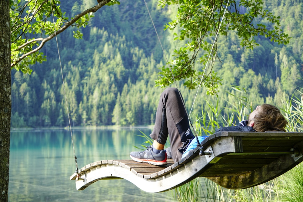 man in black jacket sitting on brown wooden boat on lake during daytime