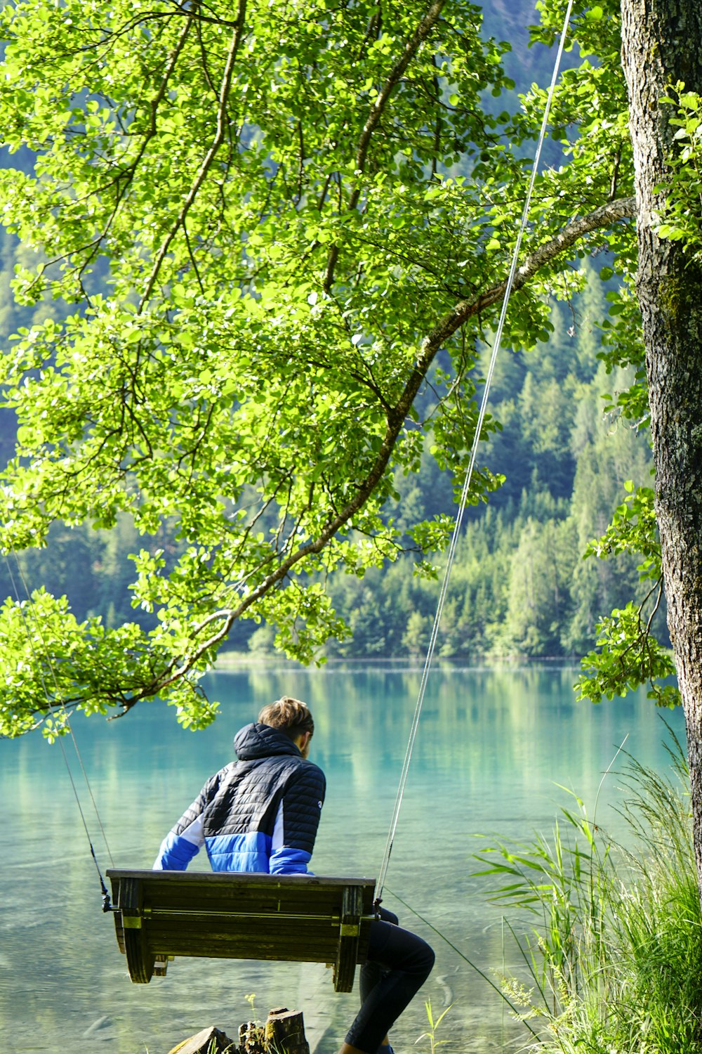 man in blue and white jacket sitting on rock near river during daytime