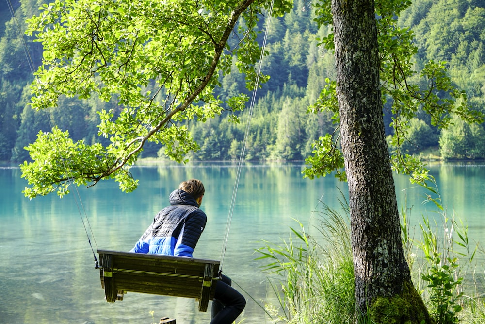 woman in white shirt sitting on brown wooden bench near lake during daytime