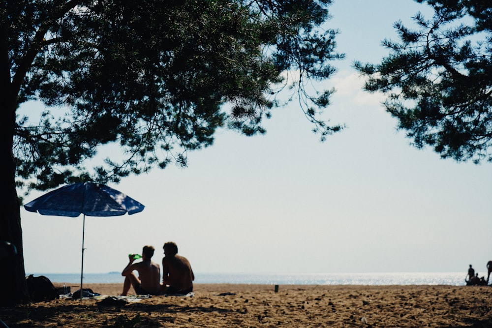 man and woman sitting on brown sand near body of water during daytime