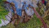 A detailed mural depicts a man wearing traditional clothing riding a horse. The background features large musical instruments, vibrant green plants, a modern building, and rural scenes with a farmhouse and people engaged in daily activities.