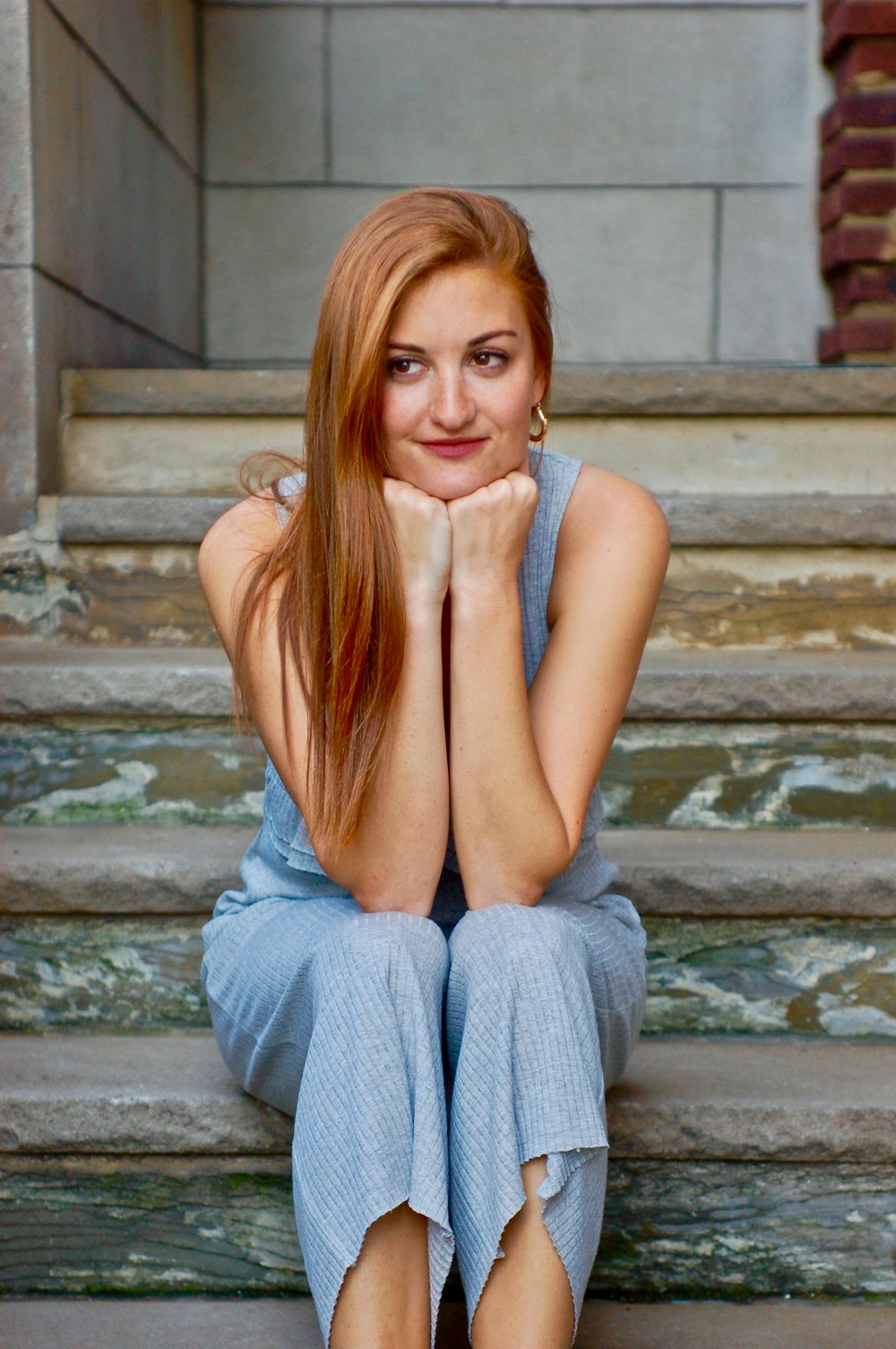 woman in gray tank top and gray pants sitting on gray concrete stairs
