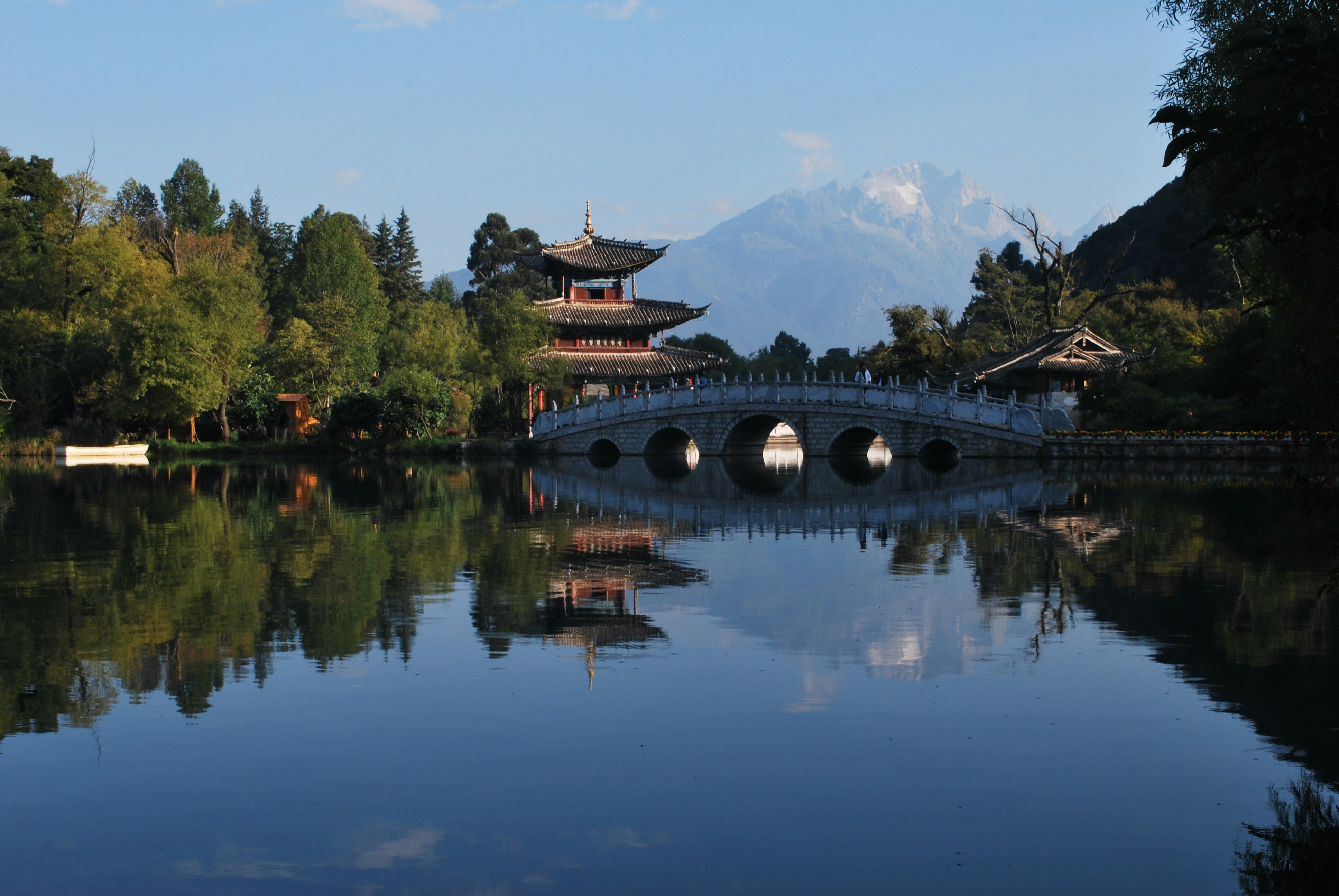 brown and black bridge over river surrounded by green trees under blue sky during daytime