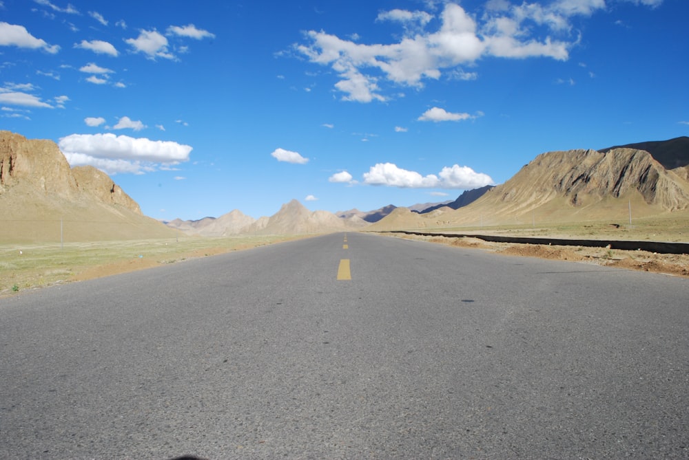 gray asphalt road near brown mountains under blue sky during daytime