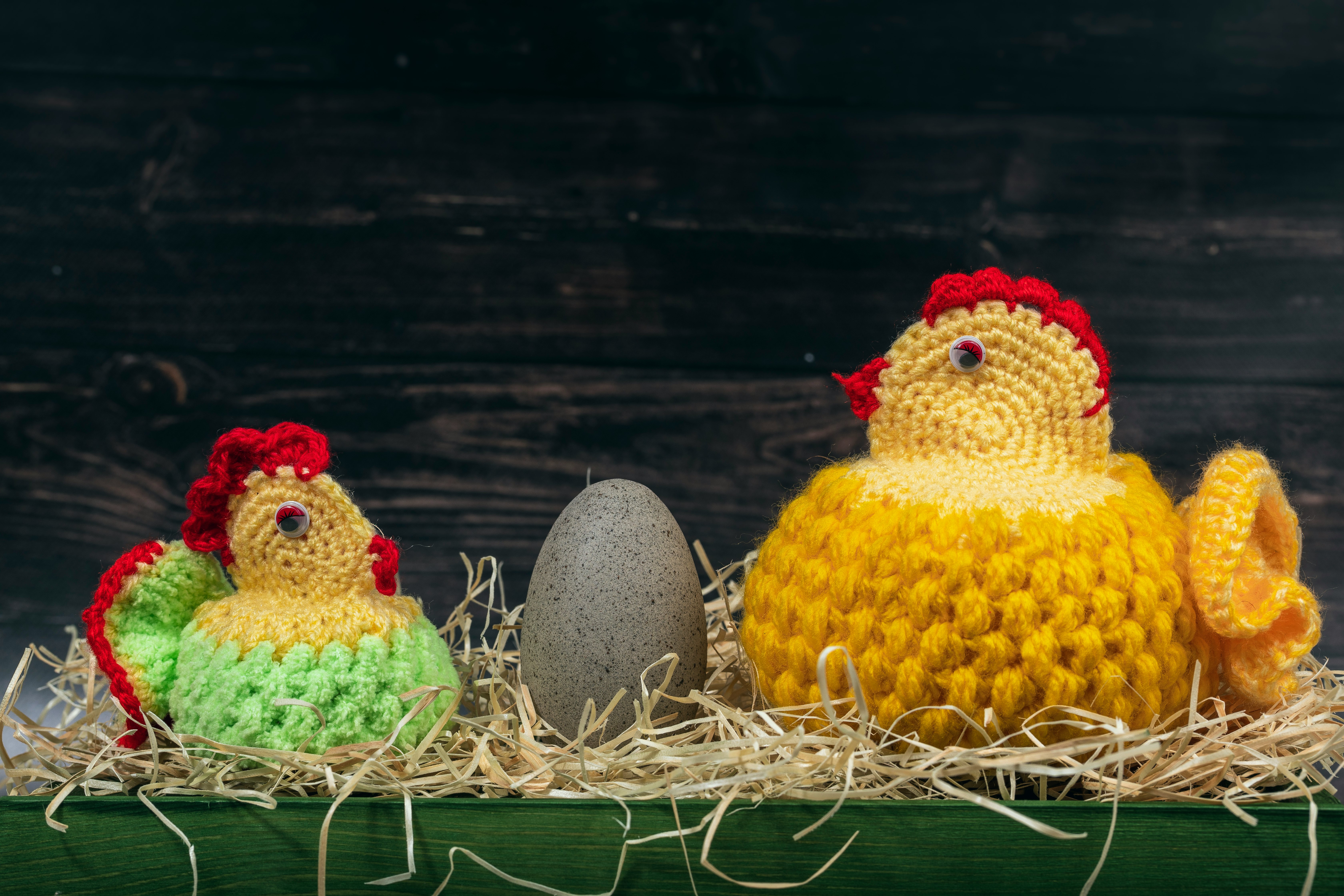Two handmade knitted woolen Easter chickens with rock egg in front of a wooden wall. Easter time.