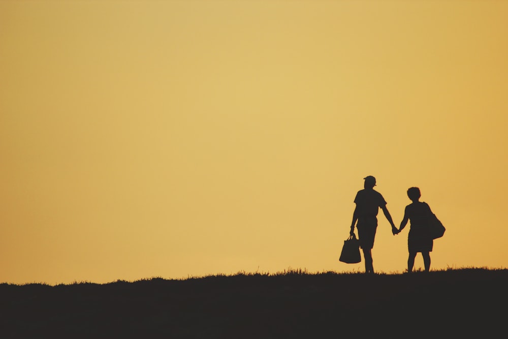 silhouette of 2 person walking on grass field during sunset