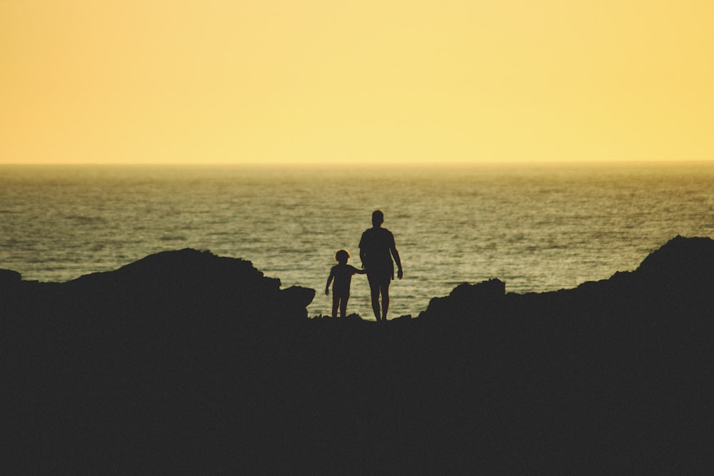 silhouette of 2 person standing on rock formation during sunset