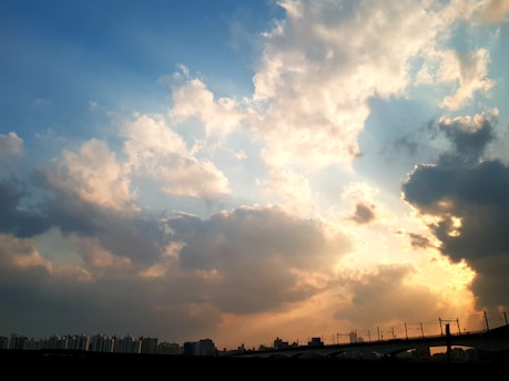 A cinematic frame capturing a golden hour cityscape with soft clouds drifting above, evoking a quiet, reflective mood.