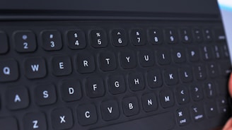 A close-up view of a black computer or tablet keyboard, showing keys arranged in a standard QWERTY layout. The keys have a slightly rounded shape, and the letters and symbols are printed in white.