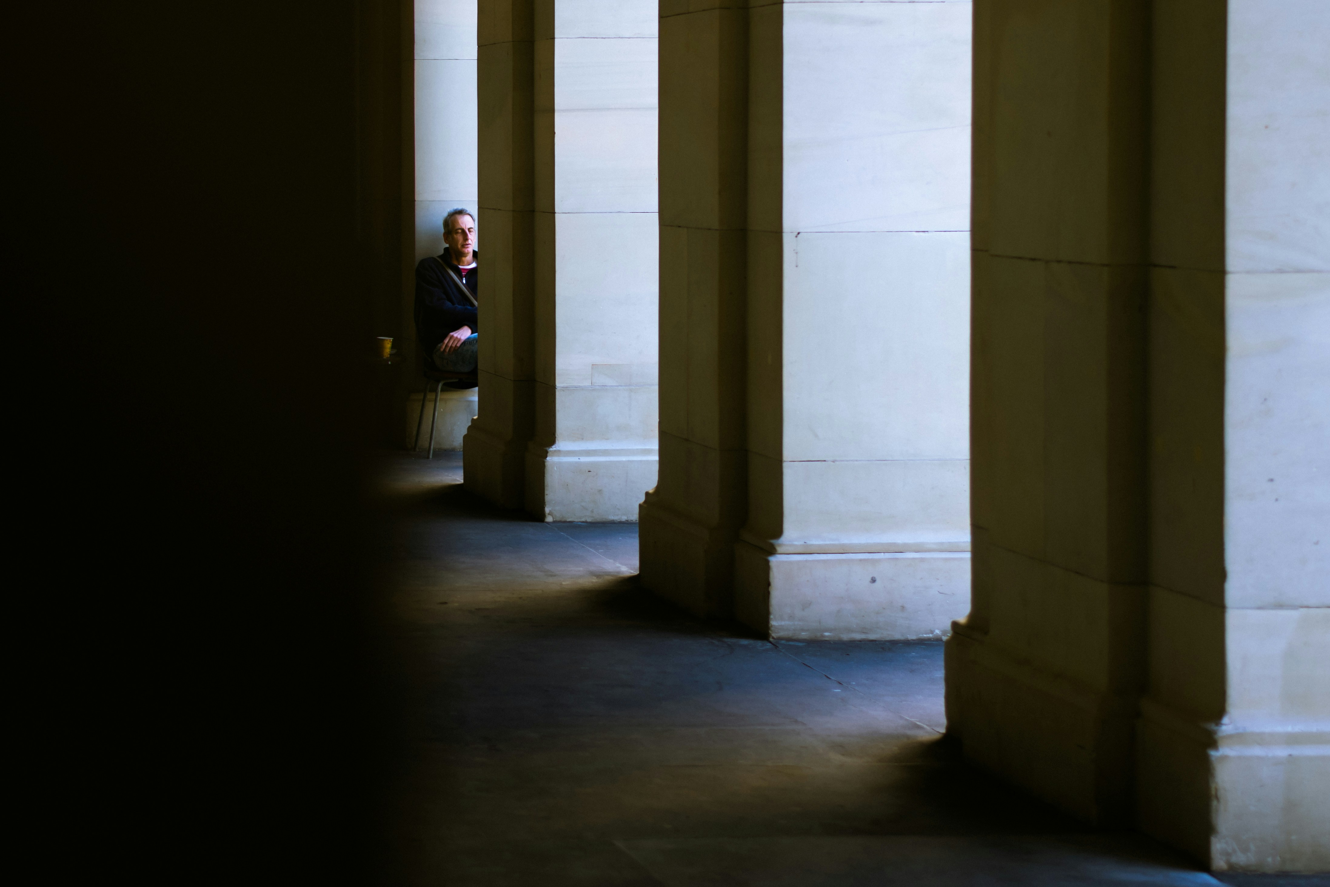 man in black jacket standing beside white concrete pillar