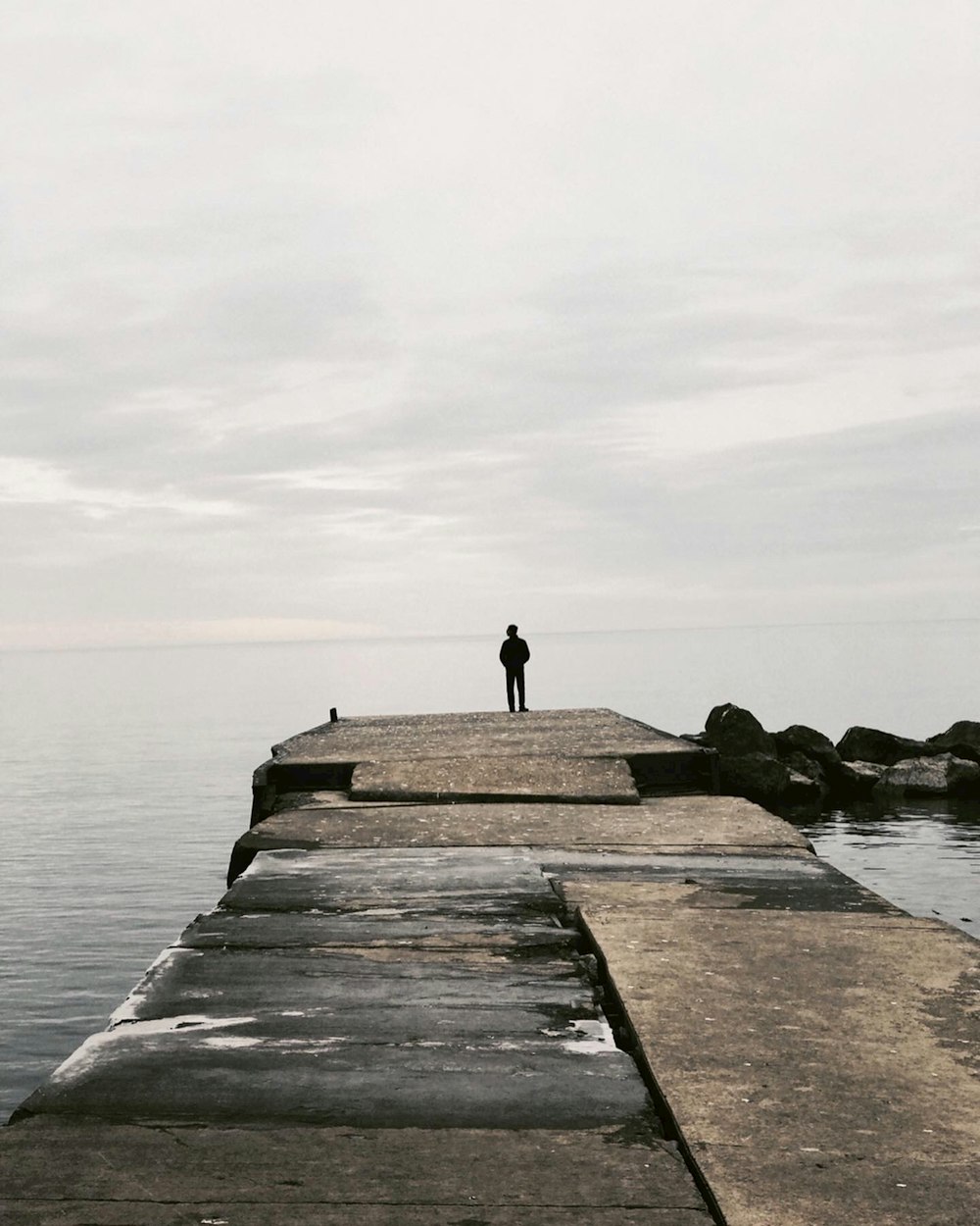 persona in piedi sul molo di cemento vicino allo specchio d'acqua durante il giorno