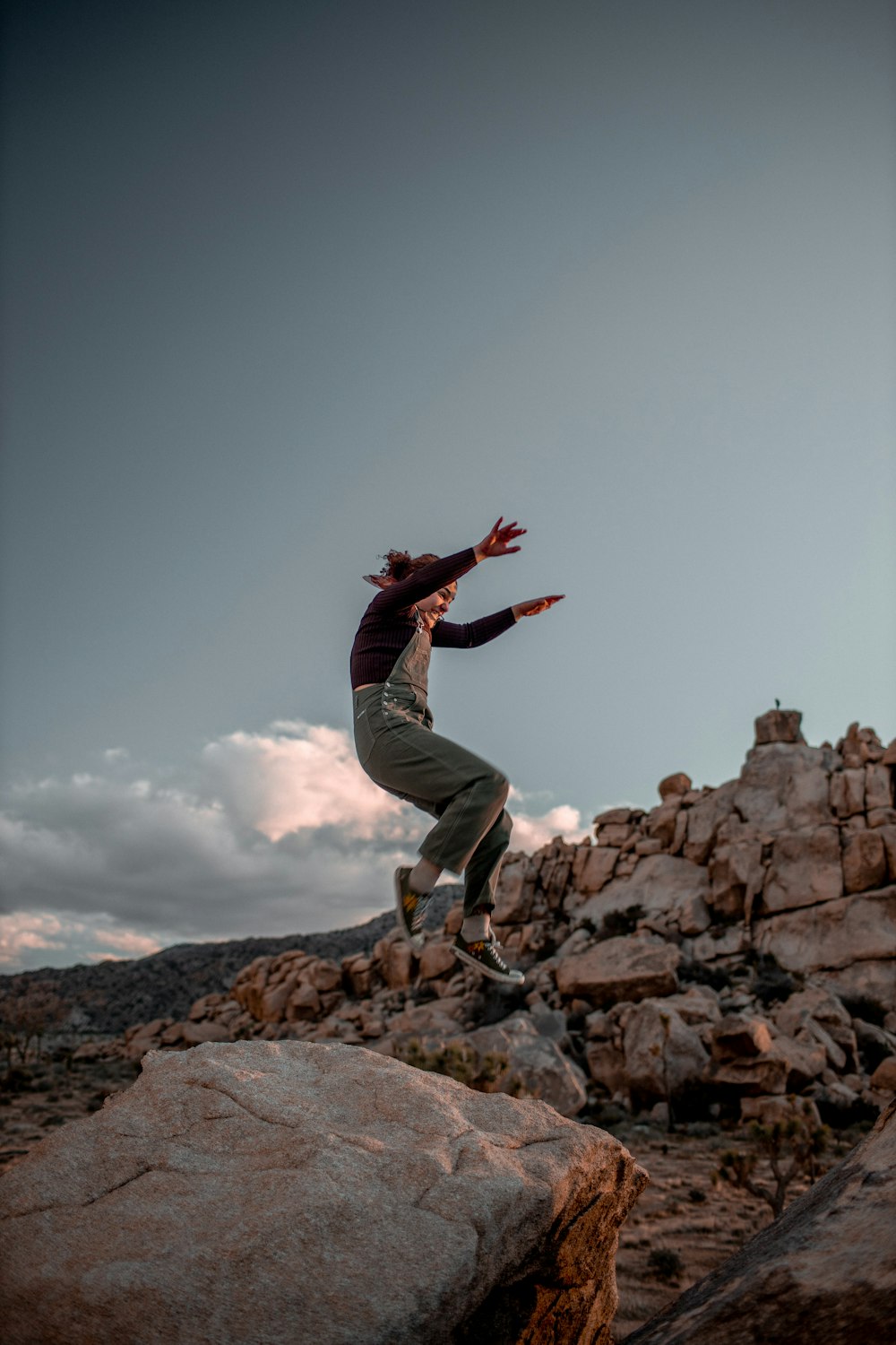 man in black jacket and gray pants jumping on brown rocky mountain during daytime