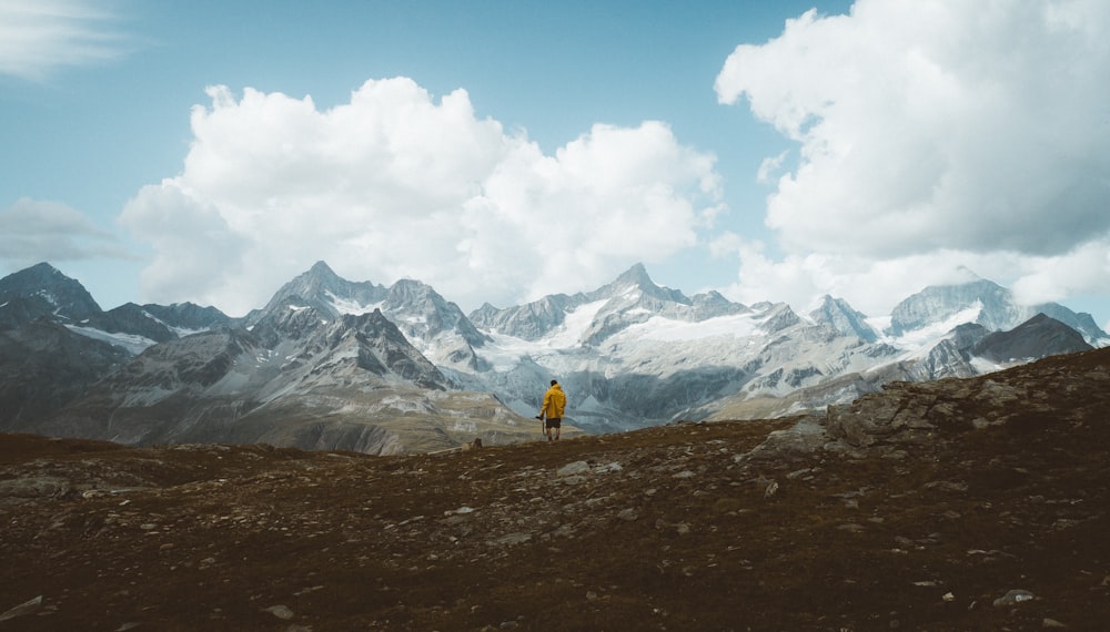 person in yellow jacket walking on brown field near snow covered mountain during daytime