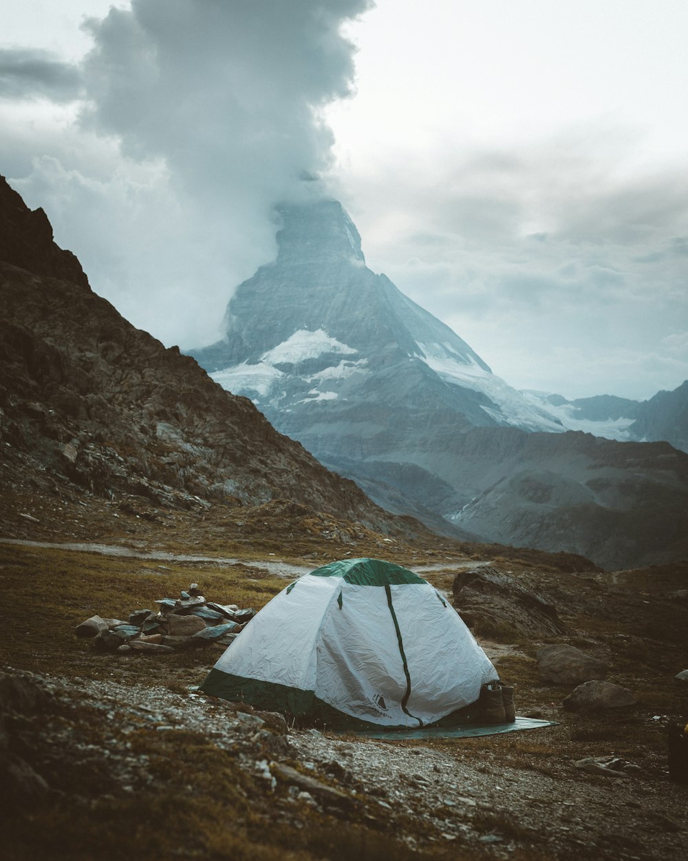 tente verte sur un champ brun près de la montagne sous des nuages blancs pendant la journée