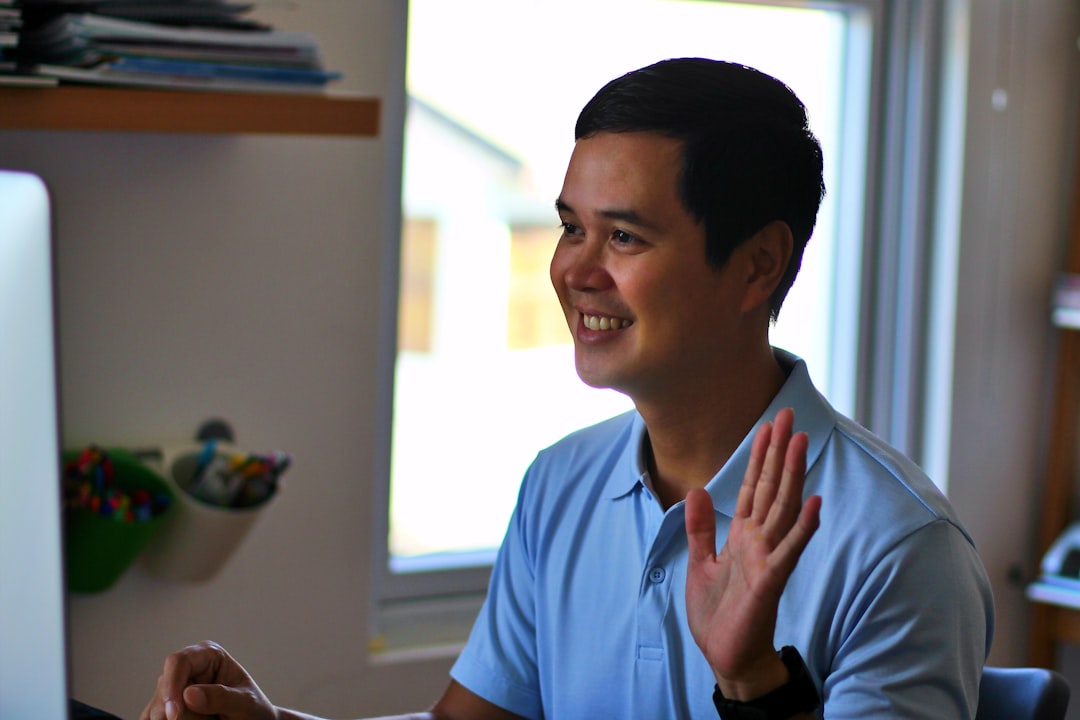 man in blue polo shirt smiling, asian male work from home online meeting