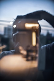 Portrait of a man framed by reflective glass surfaces amid the urban environment at dusk.