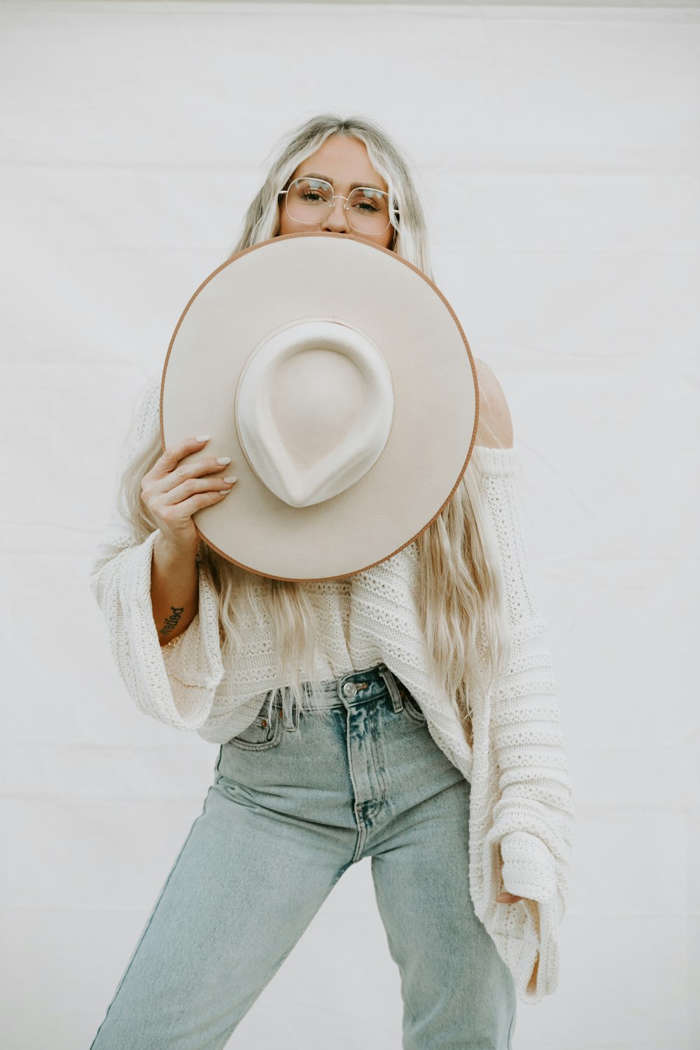 woman in white sweater and blue denim jeans holding white fedora hat