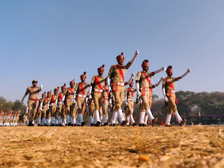 A group of students in drill team uniforms practicing precise formations on a sunny field.