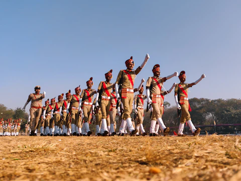 A group of students in drill team uniforms practicing precise formations on a sunny field.