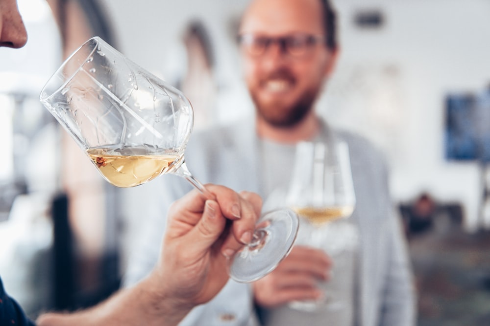 uomo in maglione bianco che tiene il bicchiere di vino chiaro