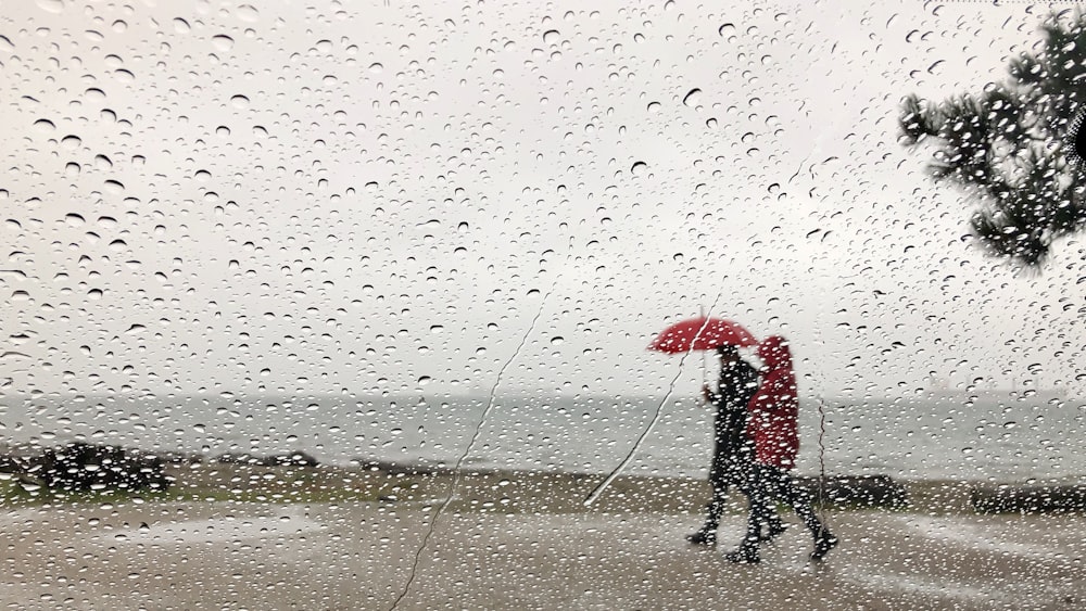 person in black jacket holding red umbrella walking on wet sand during daytime