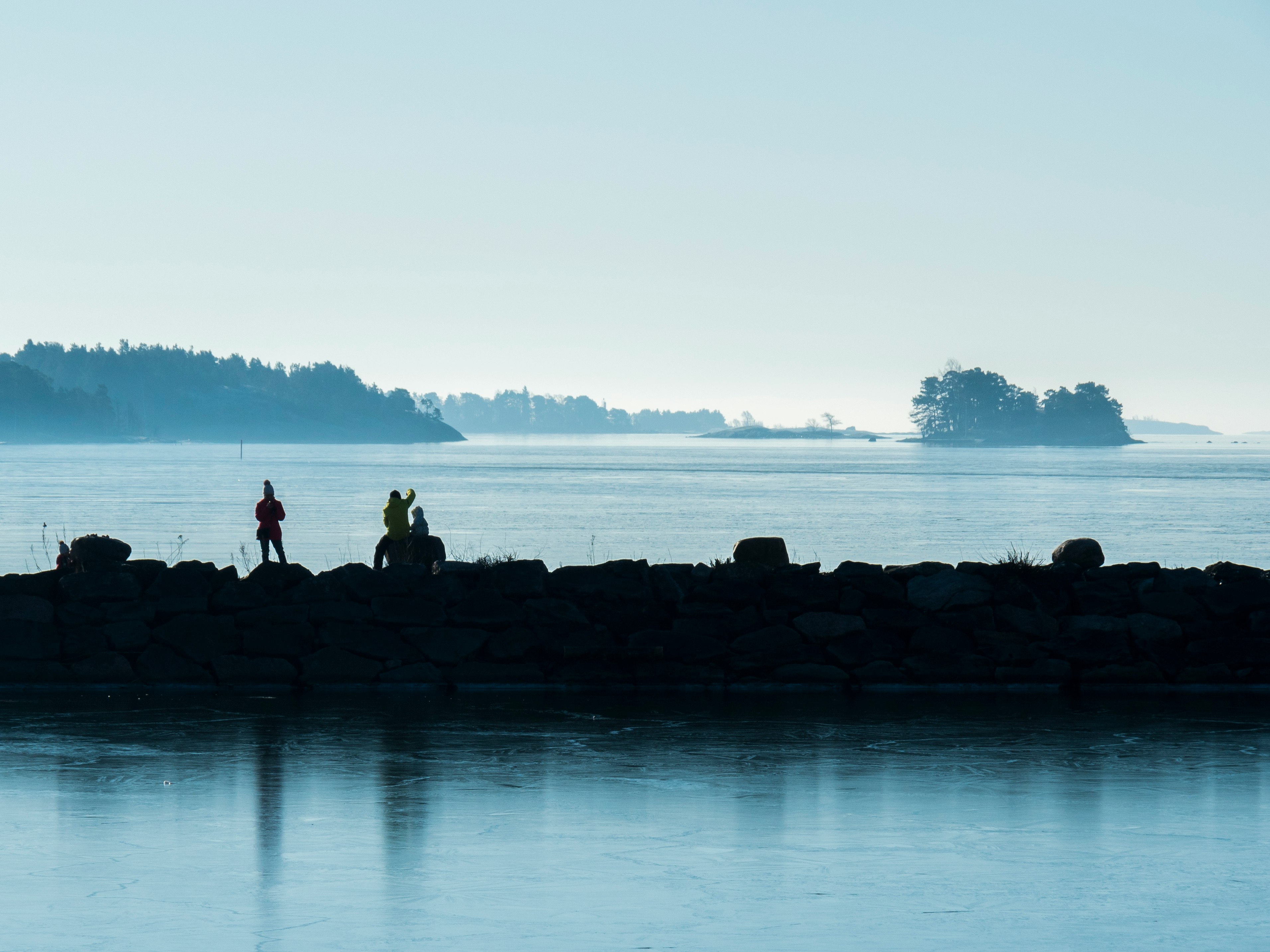 silhouette of people sitting on rock near body of water during daytime
