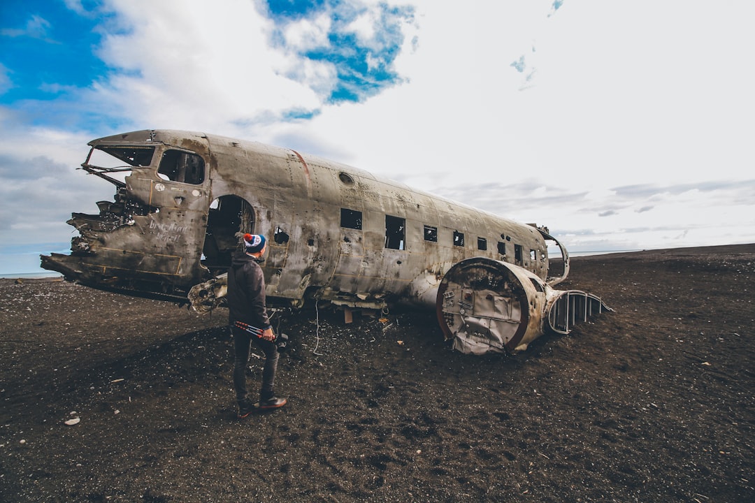 man in black jacket standing beside white and black airplane under blue and white sunny cloudy