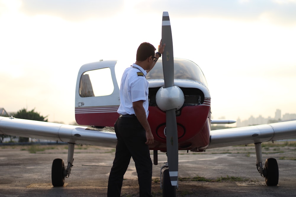 man in white t-shirt and black pants standing beside white airplane during daytime