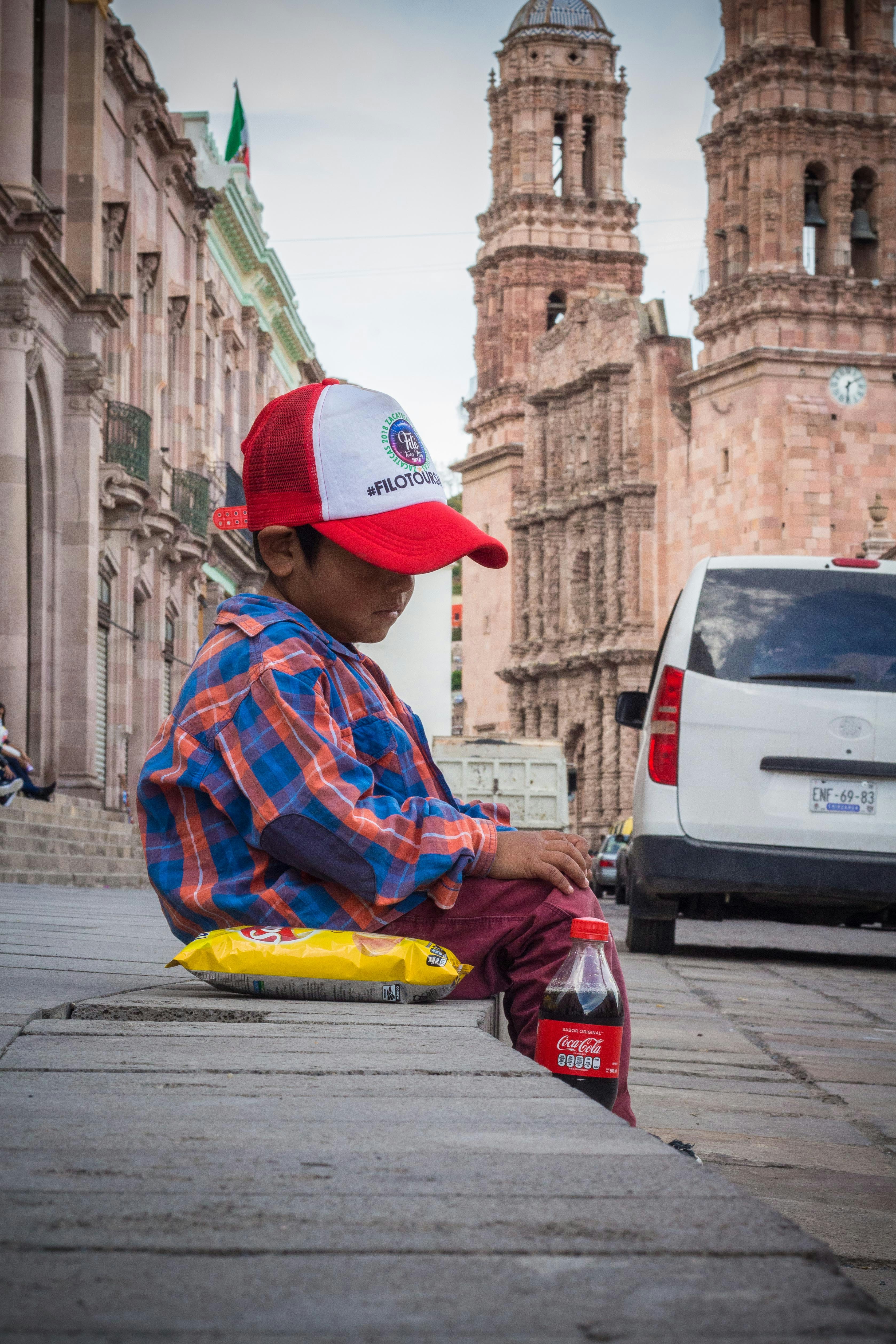 man in red and blue plaid dress shirt sitting on sidewalk during daytime