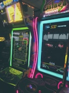 An arcade game setting with vibrant neon lighting, featuring classic game cabinets like Pac-Man and Galaga. The display screens show the game demos, and there are colorful lights around the edges of the machines.