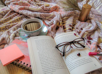 A cozy scene featuring a steaming cup of coffee in a floral-themed tumbler beside a soft pink journal.