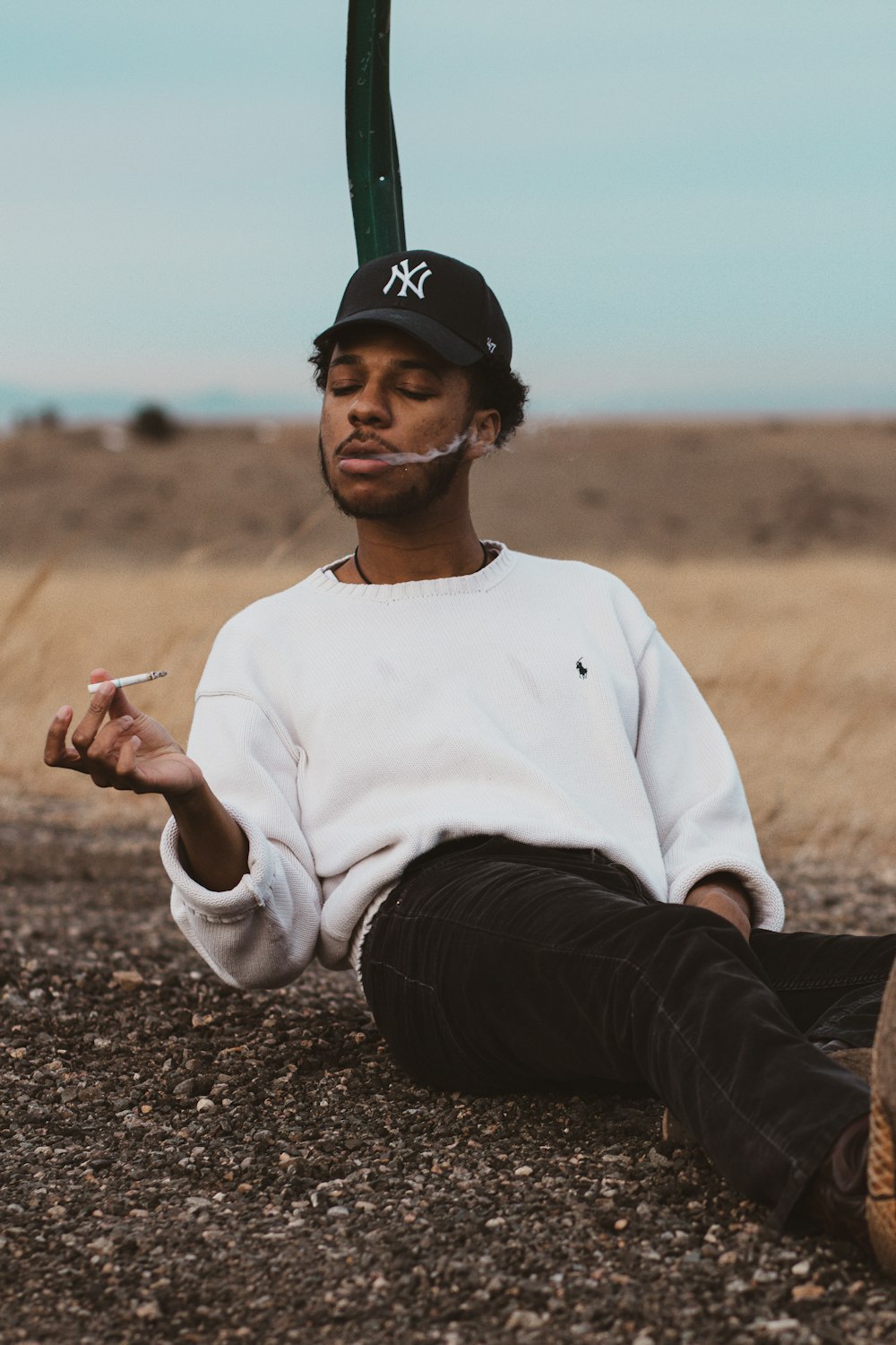 man in white crew neck long sleeve shirt and black pants sitting on brown ground during