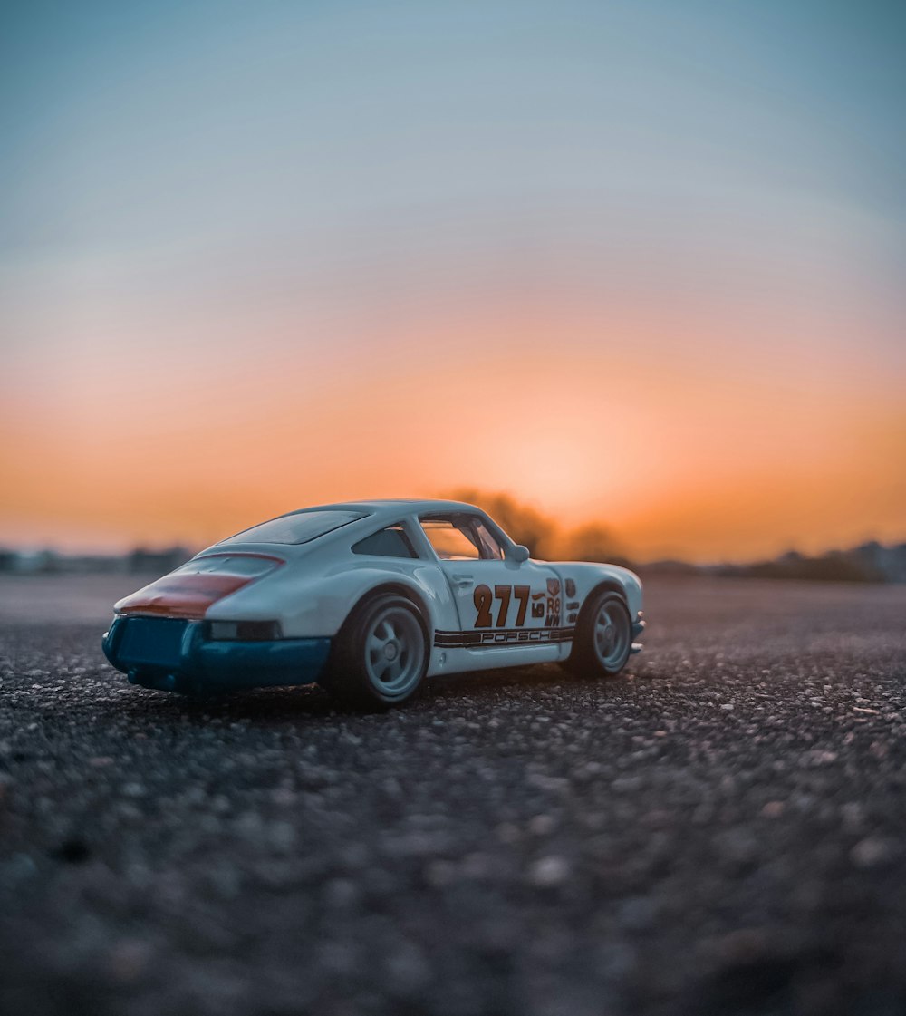 blue and white porsche 911 on gray sand during sunset