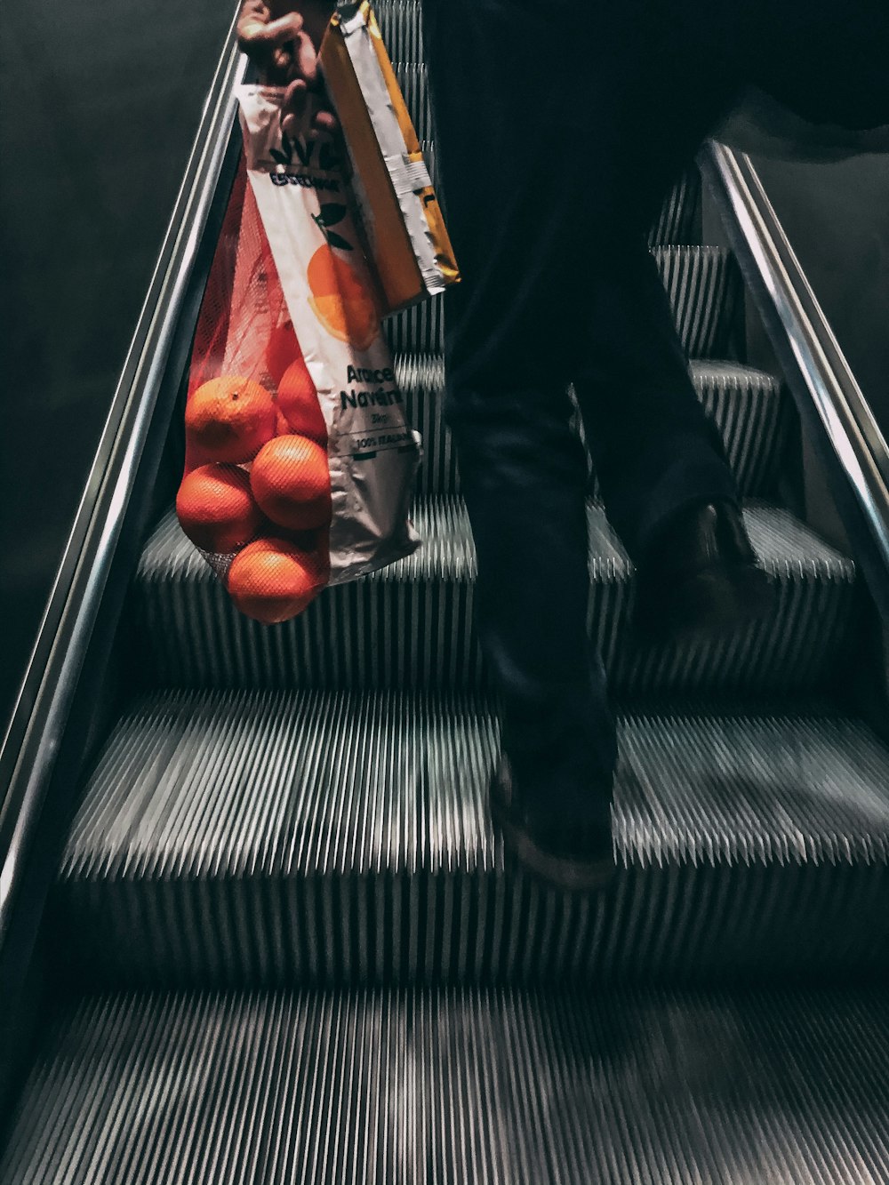 person in black pants and black leather boots on escalator