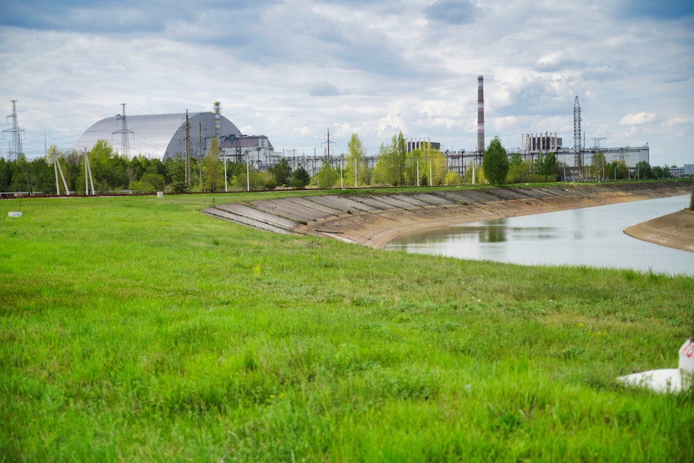 Grünes Grasfeld in Flussnähe tagsüber unter weißen Wolken